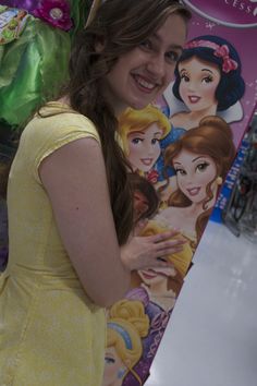 a woman in a yellow dress standing next to a sign with princesses on it