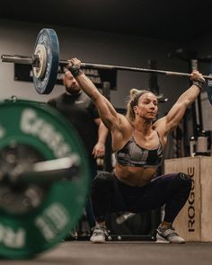 a woman doing squats with a barbell in her hands while another man watches