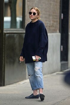 a woman in black sweater and ripped jeans walking down the street