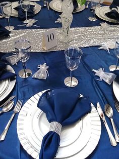 the table is set with silverware and blue linens for an elegant dinner party