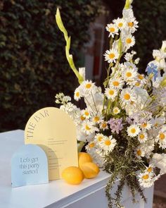 a vase filled with white flowers and daisies on top of a table next to a sign