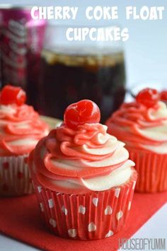 three red cupcakes with white frosting and cherries sitting on a napkin