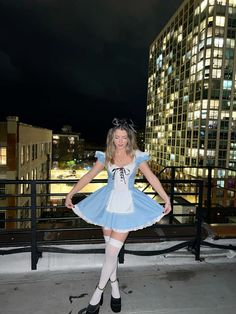 a woman dressed as alice in front of a cityscape at night with her hands on her hips