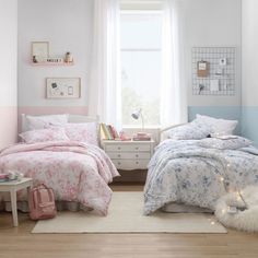 two beds in a bedroom with pink and blue decor on the walls, white rugs and light wood flooring