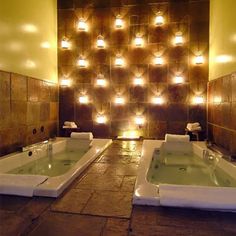 a couple of bath tubs sitting in a room with lights on the wall behind them