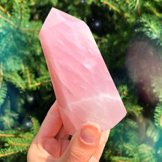 a hand holding a pink rock in front of a christmas tree