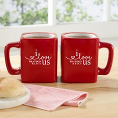 two red coffee mugs with i love us written on them next to some rolls