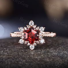 an engagement ring with a large red stone surrounded by small white diamonds on top of a rock