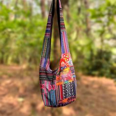 a multicolored bag hanging from a tree in front of some trees and dirt