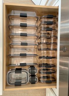 an organized kitchen drawer with clear plastic containers and black lids on the bottom, and stainless steel handles