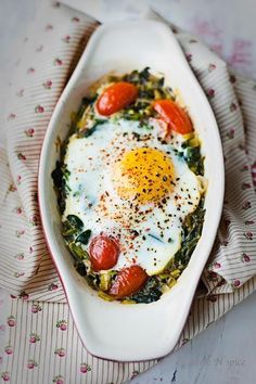 an egg in a white dish with tomatoes and spinach on top, next to a napkin