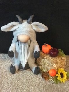 a stuffed goat sitting next to some hay and pumpkins on the ground with sunflowers