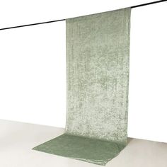 a green cloth hanging from a clothes line on top of a white floor in front of a wall