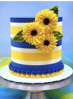 a blue, yellow and white striped cake with sunflowers on the top tier