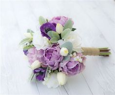 a bridal bouquet with purple flowers and greenery on a white wooden surface,