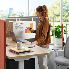 a woman standing in front of a desk with a laptop computer on top of it