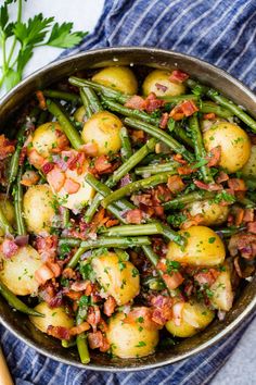 potatoes and green beans with bacon in a skillet on a blue towel next to parsley