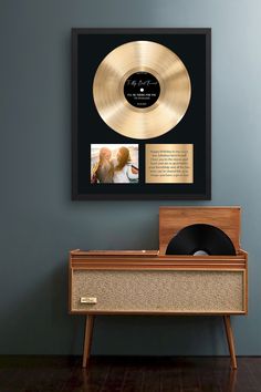 a gold record sitting on top of a wooden table next to a black framed album