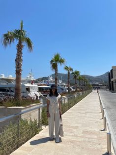 a woman walking down a sidewalk next to palm trees and yachts in the background