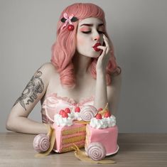 a woman with pink hair sitting at a table in front of a cake