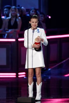 a woman in white dress holding an award on stage