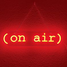 a red neon sign that says on air hanging from the ceiling in front of a red wall