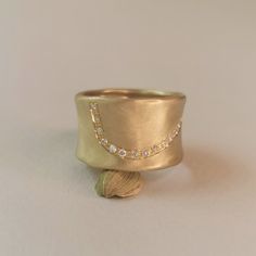 a close up of a gold ring on a white surface with a shell in the foreground