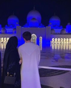 a man and woman standing in front of a white building at night with blue lights