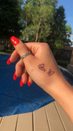 a woman's hand with a small butterfly tattoo on her left wrist, next to a swimming pool