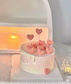 a white cake with pink hearts on it and a lit candle in the back ground