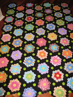 a black blanket with multicolored flowers is on the floor next to a wooden floor