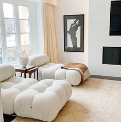 a living room filled with white furniture next to a fire place and large open windows