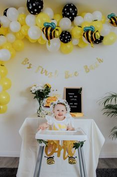 a baby sitting in a high chair next to a table with balloons and bums on it