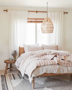 an unmade bed in front of a window with white curtains and a rug on the floor