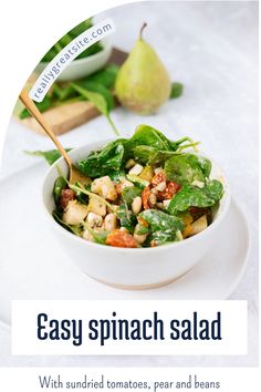 a salad with spinach, tomatoes, pears and beans in a white bowl