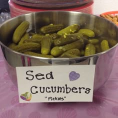 a metal bowl filled with pickles sitting on top of a pink tablecloth covered table