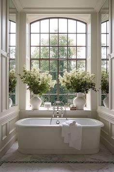 a white bath tub sitting next to two windows with vases and flowers in them