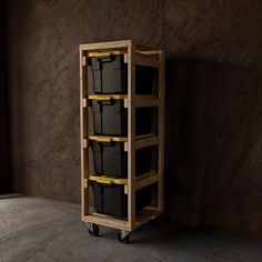 a wooden cart with three black plastic containers on it's wheels, in front of a brown wall