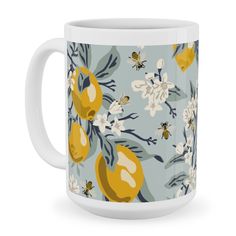 a coffee mug with yellow and white flowers on it, in front of a blue background