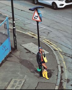 a woman in yellow rain boots talking on her cell phone next to a street sign