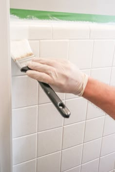 a person in white gloves is holding a paint brush and painting the wall with green tape