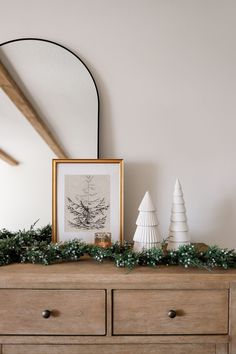 a wooden dresser topped with white christmas trees and greenery next to a framed photograph