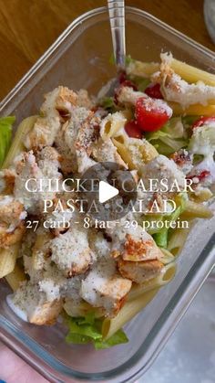 a person holding a fork in a plastic container filled with pasta and chicken salad on top of lettuce