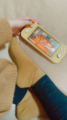 a person sitting on the floor playing with a yellow game boy handheld console controller next to their feet