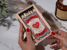 a person holding a match box with matches in it next to a candle and some feathers