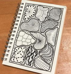 a spiral notebook with an abstract design on the front and back cover, sitting on top of a wooden table