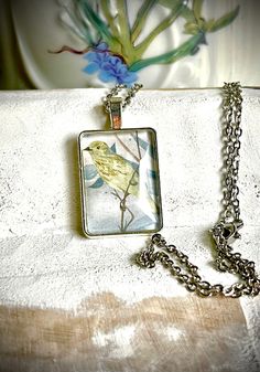 a necklace with a bird on it sitting on top of a white cloth covered table