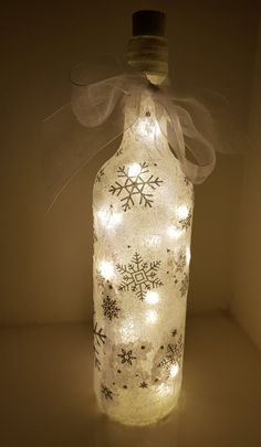 a lighted bottle with snowflakes on it and a bow hanging from the top