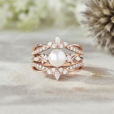 a white pearl and diamond ring sitting on top of a sand covered ground next to a pine cone