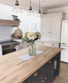 a vase with flowers sitting on top of a wooden counter in a kitchen next to an oven